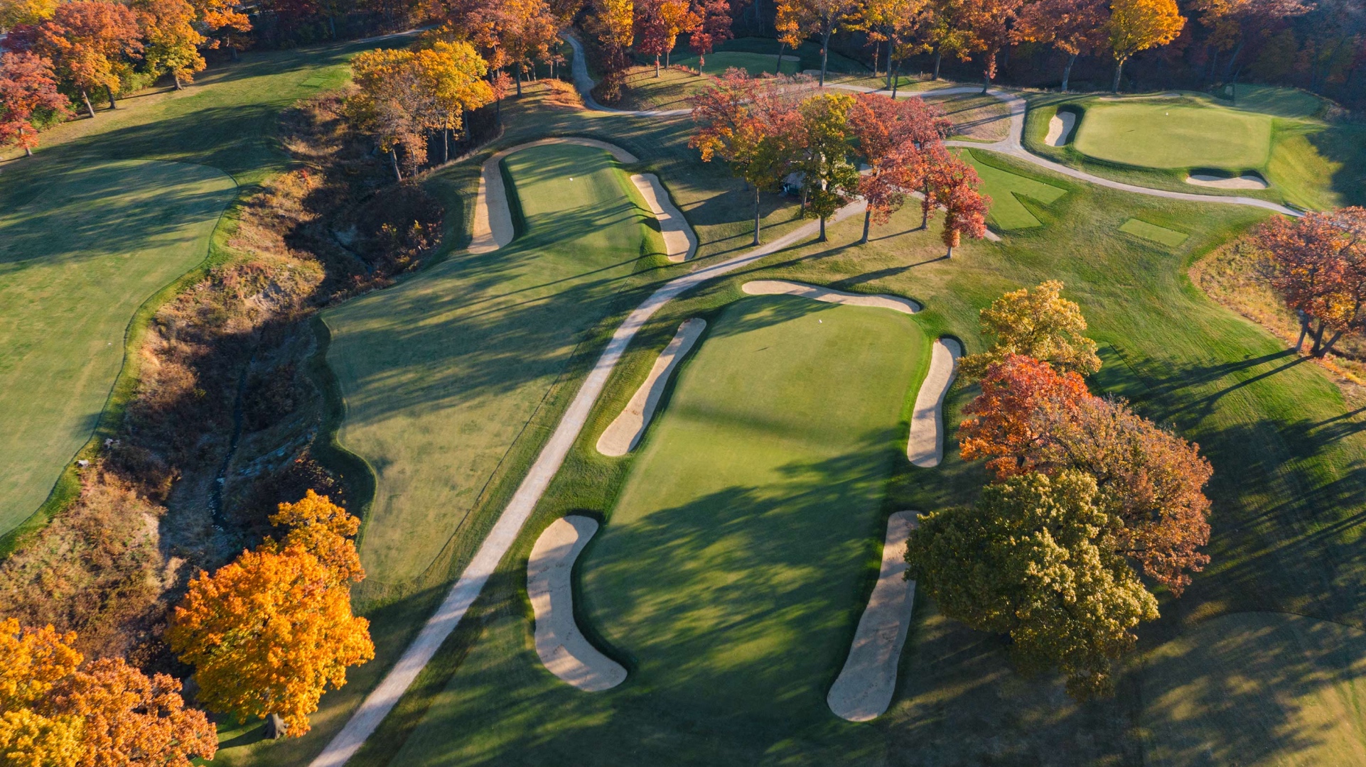 A Biarritz template green photographed in autumn light, with a deep central swale and flanking bunkers.