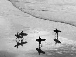 Three surfers walking across reflective wet sand in Biarritz.