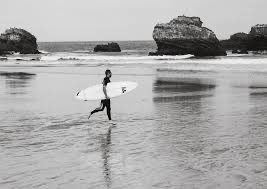 A surfer carrying a board across the wet beach at Biarritz.